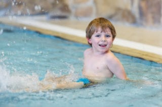 small boy smiling and splashing in swimming pool
